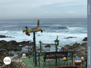 Dieses Bild vom Camino Portugues zeigt einen kleinen bunten Ruheplatz mit Bank und Flugzeug, der direkt an den Klippen gebaut ist.