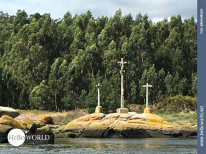 Auf der Camino Portugues Seeroute von der Ria de Arousa entlang des Flusses Rio Ulla stehen drei Kreuze auf gelblichen Felsen, im Hintergrund sind B&auml;ume.