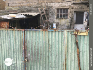 Dieses Bild vom Camino Portugues zeigt ein altes blechernes Hoftor, dahinter ein verwahrlostes Haus.