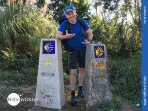 Das Bild zeigt zwei Wegweiser auf dem Camino Portugues die in unterschiedliche Richtungen weisen. Dazwischen steht Nico.