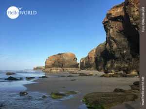 Das Bild zeigt die Steilklippen des Praia das Catedrais bei Sonnenschein und blauem Himmel.