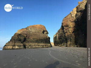 Riesige Felsen wie hier im Bild vor blauem Himmel pr&auml;gen den Praia das Catedrais.