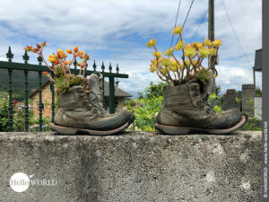 Zweckentfremdet: alte Wanderstiefel Hier sieht man eine Mauer auf der mit Blumen bepflanzte Wanderstiefel stehen in der Nähe der Ortschaft Padron.