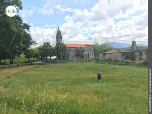 Hier sieht man Nico auf einer Wiese und im Hintergrund eine alte steinerne Kirche in der N&auml;he der Ortschaft O Campo.