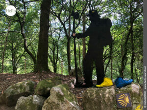 Stahl-Skulptur eines Pilgers Hier sieht man eine metallene Skulptur eines Pilgers und ein Jakobswegzeichen im Wald in der Nähe der Ortschaft Cacheiro.