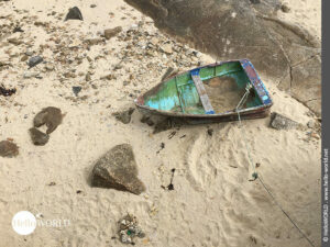 Hier sieht man ein gestrandetes kleines buntes Fischerboot am Strand.
