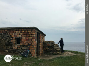 Das Bild vom spanischen K&uuml;stenweg in der N&auml;he von Pobena zeigt die Punta del Castillo Viejo,, eine alte steinerne Ruine an der Steilklippe, vor der eine Frau ins Meer blickt.