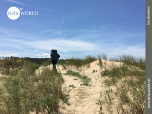 Auf und Ab in der Dünenlandschaft Nordspaniens Das Bild einer Dünenlandschaft an der spanischen Nordküste zeigt eine Frau mit Rucksack und Stöcken bepackt, wie sie über die Sandhügel geht.
