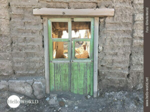 Das Bild aus einem bolivianischen Dorf zeigt eine Steinmauer mit einem T&uuml;rrahmen und einer gr&uuml;nen aus kaputten Holzleisten bestehenden T&uuml;r.