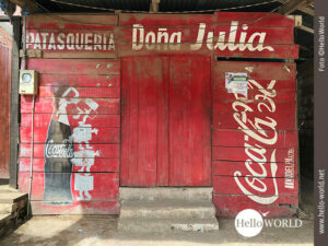 Auf diesem Bild aus Rurrenabaque, Bolivien, sieht man die Fassade einer H&uuml;tte, die aus roten Holzlatten mit CocaCola-Schriftzug und Flaschenabbildung besteht.