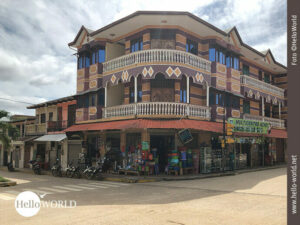 Auf diesem Foto von Rurrenabaque, Bolivien, sieht man ein buntes Eckhaus mit Balkongel&auml;nder und im Untergeschoss eine Art Supermarkt.