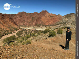 Berglandschaft in Bolivien Das Bild aufgenommen in Tupiza, Bolivien, zeigt den Blick auf das Tal bei Palala, mit seinen roten Bergen und im Vordergrund eine schwarz gekleidete Wanderin.