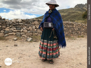 Dieses Bild zeigt eine alte Peruanerin im Colca Canyon-Gebiet, die einen bunten Hut und ein blaues Tuch tr&auml;gt und um die Schulter ein Radioger&auml;t.