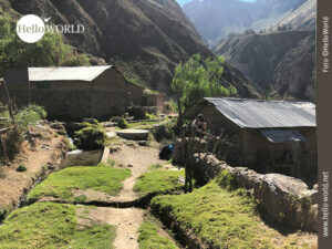 Das Bild zeigt ein paar H&auml;user, die im Colca Canyon, Peru, stehen, einger&auml;hmt von Felsw&auml;nden, davor ein Weg und ein kleiner Bachlauf.