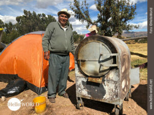 Das Bild aus Cusco, Peru, zeigt einen Mann neben einem alten Ofen auf einem Acker, in dem Cuy zubereitet wird.