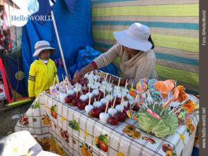 Dieses Bild vom Sonnenfest in Cusco, Peru, zeigt einen Stand mit kandierten &Auml;pfeln an dem ein Kind steht und gespannt auf die Auslage sieht.